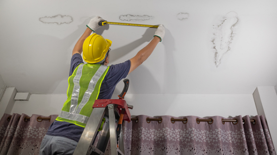Image shows construction worker assessing leak in ceiling.
